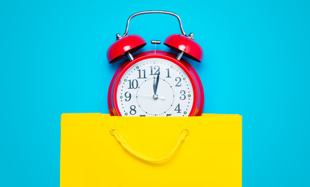 red alarm clock in the beautiful yellow shopping bag on the wonderful blue backgroundの写真素材