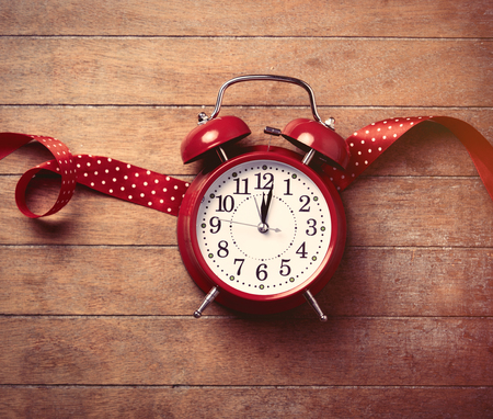 beautiful alarm clock and red ribbon lying on the woderful brown wooden background
