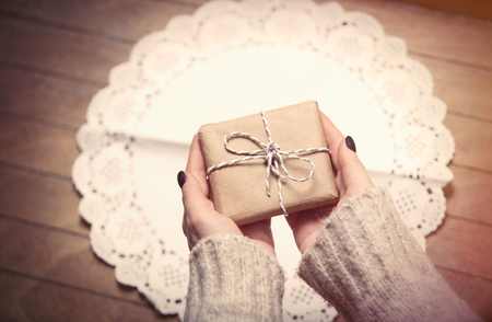 beautiful woman hands holding cute gift on the wonderful brown wooden backgroundの写真素材