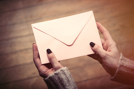 beautiful woman hands holding big white envelope on the wonderful brown wooden backgroundの写真素材