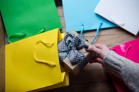 beautiful woman hands holding cute gift and putting it inside one of the shopping bags on the wonderful colorful shopping backgroundの写真素材