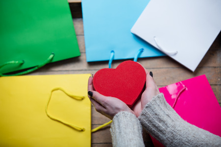beautiful woman hands holding heart shaped toy on the wonderful colorful shopping bag backgroundの写真素材