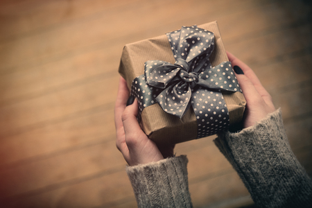 beautiful woman hands holding cute blue gift on the wonderful brown wooden backgroundの写真素材