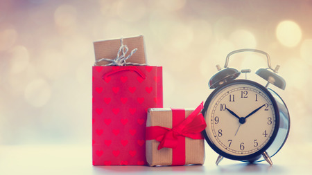 cool shopping bag, black alarm clock and beautiful gifts on the fairy lights bokeh backgroundの写真素材