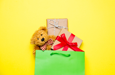 cute gifts in beautiful green shopping bag and teddy bear on wonderful yellow backgroundの写真素材