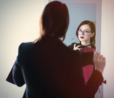 beautiful young woman standing in front of mirror, choosing what to wear and looking at her reflectionの写真素材