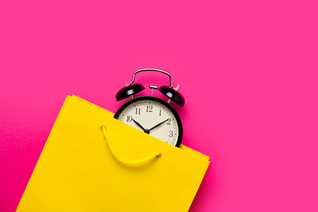 cool black alarm clock in beautiful yellow shopping bag on the wonderful pink backgroundの写真素材