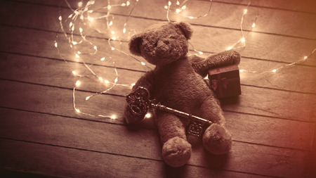 cute fluffy teddy bear with gift and golden key and bright garland on the wonderful brown wooden backgroundの写真素材