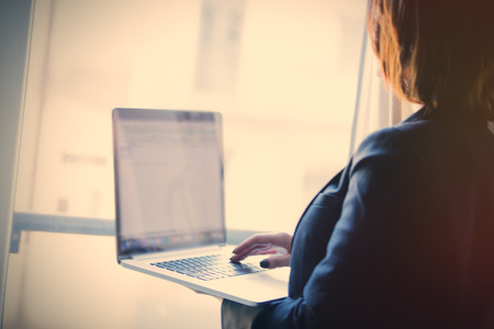 young beautiful woman holding a notebook and typing text near the windowの写真素材
