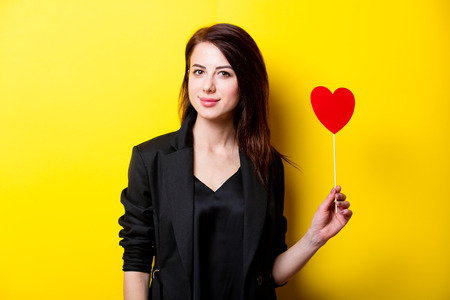 beautiful young woman with heart shaped toy standing in front of wonderful yellow backgroundの写真素材