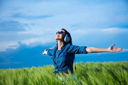 beautiful young woman in earphones standing in the middle of the wonderful green fieldの写真素材