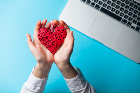 white caucasian female hands holding heart shaped toy near laptop on the wonderful blue backgroundの写真素材