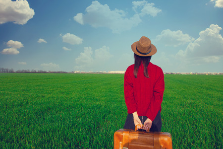 beautiful young woman standing on the grass with suitcase on the wonderful green fieldの写真素材