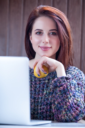 beautiful young woman holding apple near her laptop on the wonderful brown wooden backgroundの写真素材