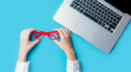white caucasian female hands holding red glasses near laptop on the wonderful blue backgroundの写真素材