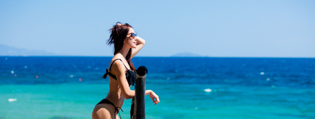 beautiful young woman standing near wooden fence and looking at the sea in Greeceの写真素材
