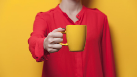 beautiful young woman hand holding a yellow cup of the wonderful yellow backgroundの写真素材