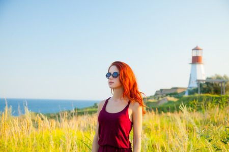 beautiful young woman standing in front of wonderful sea and lighthouse backgroundの写真素材