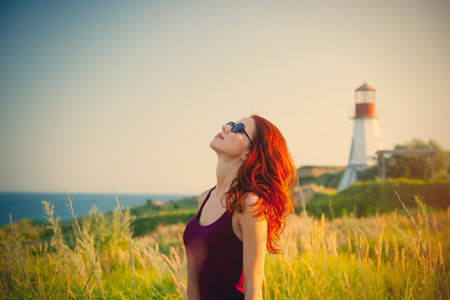 beautiful young woman standing in front of wonderful sea and lighthouse backgroundの写真素材