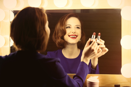 photo of beautiful young woman holding her lipstick near the window with lightsの写真素材