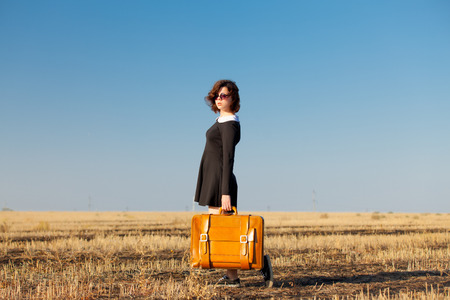 photo of beautiful young girl standing with suitcase in the fieldの写真素材