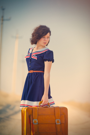 photo of beautiful young girl standing with suitcase on the road in the fieldの写真素材