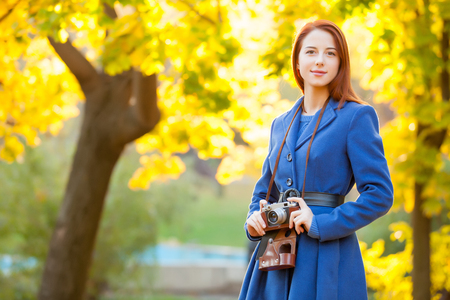 photo of young woman with retro camera on the wonderful autumn trees backgroundの写真素材
