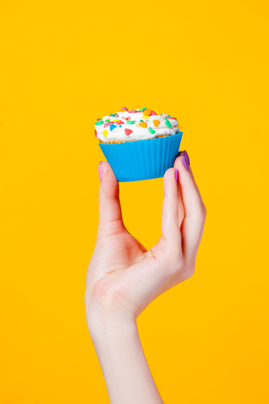 photo of female hand holding cupcake on the wonderful yellow backgroundの写真素材