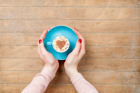 photo of female hands holding cup of coffee on the wonderful brown wooden backgroundの写真素材