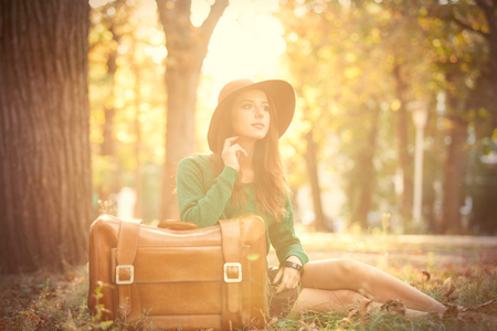 photo of beautiful young woman with suitcase on the wonderful autumn park backgroundの写真素材