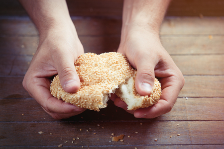 photo of male hand touching fresh bun with sesame on the wonderful brown wooden backgroundの写真素材