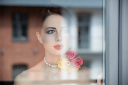 portrait of beautiful young woman standing near the window and looking at somethingの写真素材