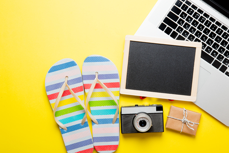 photo of empty blackboard, colorful sandals, retro camera, cute gift and cool laptop on the wonderful yellow studio backgroundの写真素材