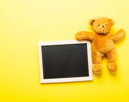 photo of empty blackboard and cute teddy bear on the wonderful studio yellow backgroundの写真素材