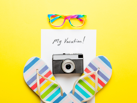 photo of sheet of paper My Vacation, colorful glasses and colorful sandals, retro camera  on the wonderful yellow studio backgroundの写真素材