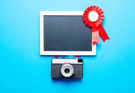 photo of red prize ribbon, retro camera and empty blackboard on the wonderful blue studio backgroundの写真素材