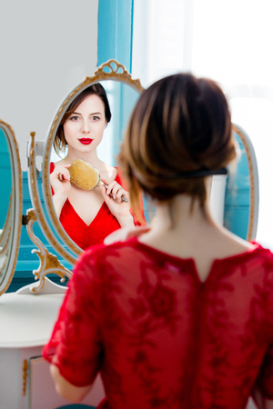 portrait of beautiful young woman with comb looking at herself in the wonderful mirror and sitting next to itの写真素材