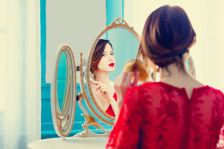portrait of beautiful young woman with comb looking at herself in the wonderful mirror and sitting next to itの写真素材