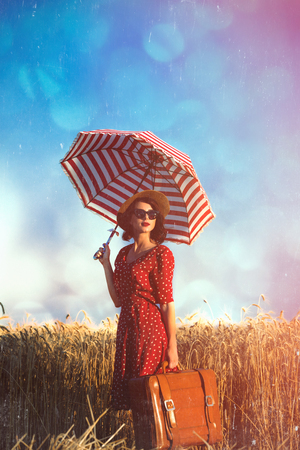 photo of beautiful young woman with umbrella and suitcase on the wonderful field and sky backgroundの写真素材