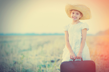 photo of beautiful girl holding suitcase and standing in the field on the wonderful sky backgroundの写真素材
