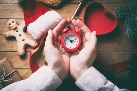 Young woman hands wrapping christmas alarm clock and gifts on wooden background, Photo in old color...