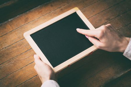 Young woman hands holding little board on wooden background, Half side viewの写真素材