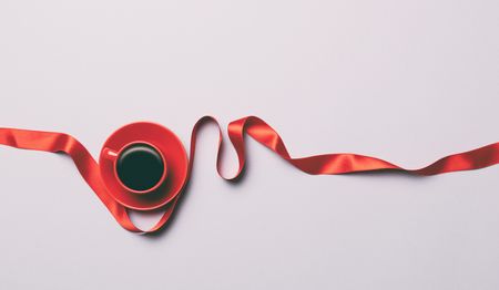 Cup of coffee and red twisted bow on grey background