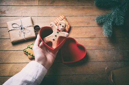 Young woman hand holding christmas gingerbread man cookie on wooden background, Photo in old color image styleの写真素材