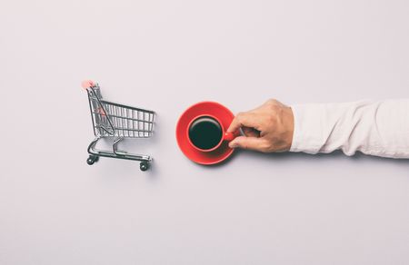 Man holding red cup of coffee near shopping cart on grey backgroundの写真素材
