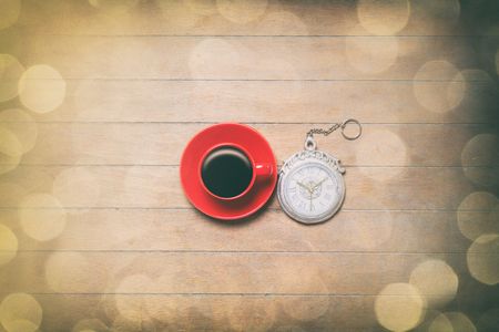 Red Cup of coffee with watch and bokeh on wooden backgroundの写真素材