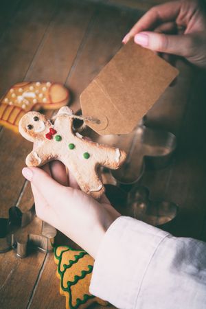 Young woman hands holding christmas gingerbread man cookie and prise tag on wooden background, Photo in old color image styleの写真素材