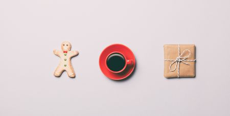 Red cup of coffee and cookie with box on grey background, view above