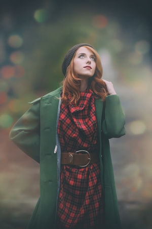 Portrait of young redhead woman in green coat in autumn park with bokehの写真素材