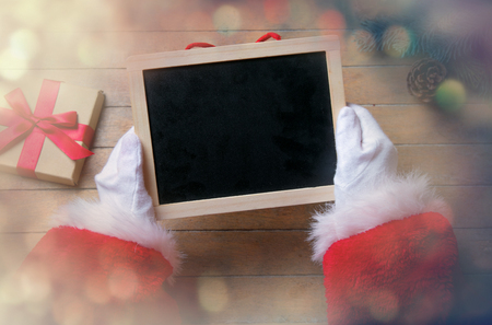 Santa Claus holding black board on wooden background with bokehの写真素材